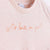 Detalle de texto estampado en color naranja. Camiseta rosa de algodón orgánico para niños, estampado a mano con tintas ecológicas. Modelo unisex.